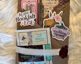 May include: A brown paper package with stickers that read "In my Bookish Era" and "Cauldron Blessed." It includes tea sachets, a ribbon, and a wax seal. The word "Fantasy" is stamped on the bottom.