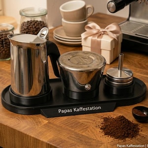 Könnte beinhalten: Ein schwarzes, ovales Kaffee-Organizer-Tablett mit dem aufgedruckten Text Papas Kaffestation auf der Vorderseite. Das Tablett enthält ein Milchkännchen aus Edelstahl, einen Moka-Kannen-Boden und einen kleinen Metallbehälter mit Deckel.