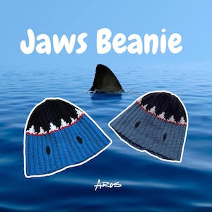 Può includere: Due berretti lavorati a maglia, uno blu e uno grigio, con un design ispirato agli squali. I berretti hanno una parte superiore nera con accenti bianchi e rossi e un dettaglio a bocca di squalo. Il testo "Jaws Beanie" è visualizzato sopra i berretti.