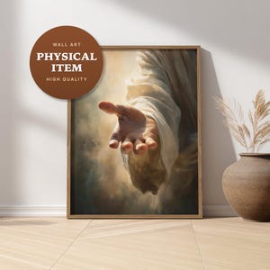 May include: A framed wall art print featuring a realistic painting of an outstretched hand reaching forward from a draped sleeve. The artwork displays soft, warm lighting against a cloudy, ethereal background with a brown circular badge.