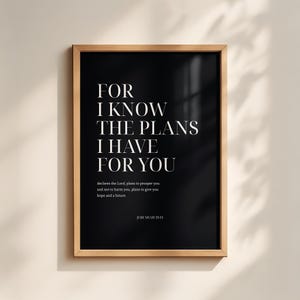 May include: A rectangular wall art print in a light wood frame featuring a black background with white text that reads: FOR I KNOW THE PLANS I HAVE FOR YOU, declares the Lord, plans to prosper you and not to harm you, plans to give you hope and a future. JEREMIAH 29:11.