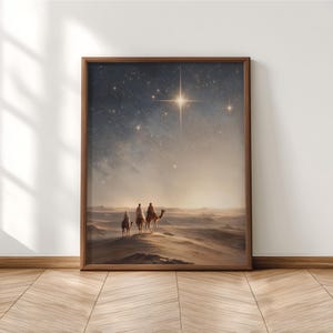 Könnte beinhalten: Ein gerahmter Druck zeigt drei Figuren auf Kamelen in einer Wüstenlandschaft unter einem sternenklaren Nachthimmel. Ein heller Stern leuchtet darüber. Das Kunstwerk ist in einem braunen Holzrahmen gerahmt.