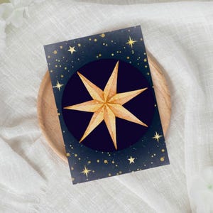 Könnte beinhalten: Eine Grußkarte mit einem goldenen Sternenmuster auf marineblauem Hintergrund, verziert mit goldenen Sternen und Punkten. Der Sternenmuster befindet sich mittig in einem dunkelblauen Kreis. Die Karte liegt auf einem Holztablett.