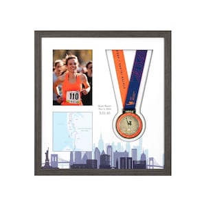 Può includere: Esposizione incorniciata con una maratoneta con una maglia arancione, una mappa della gara e una medaglia. La medaglia ha una finitura dorata con un disegno della Statua della Libertà. La cornice include uno skyline di New York.