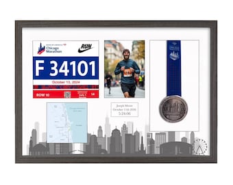 May include: A dark wood-framed display case featuring a Chicago Marathon race bib with the number F 34101, a photograph of a runner, a blue medal with a ribbon, a map of the course, and a plaque reading Joseph Moore October 11th 2026 5:24:06.