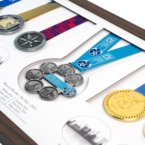 Puede incluir: Un marco de madera para exhibir varias medallas de marat&oacute;n con cintas de colores. En el centro, una medalla Six Star con una cinta azul. El texto en el paspart&uacute; blanco dice: Marcus Brooke - Six Star - 2025, Berlin 2025, Boston 2025, Chicago 2024, London 2025, New York 2024, Tokyo 2024.