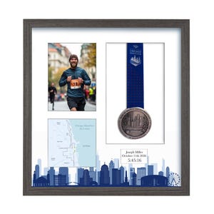 Puede incluir: Un marco gris oscuro que contiene una foto de un corredor, una medalla del marat&oacute;n de Chicago con cinta azul, un mapa de la ruta de 26.2 millas y una placa blanca con el texto Joseph Miller, October 11th 2026, 5:45:16 sobre un horizonte azul.