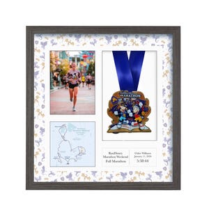 May include: Framed display featuring a marathon medal, a runner, and a race map. The medal has a blue ribbon and a colorful design. The frame is gray with a patterned border. The text on the frame reads "RunDisney Marathon Weekend Full Marathon".