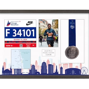 May include: A dark wood-framed display case featuring a Chicago Marathon race bib with number F 34101, a photograph of a runner, a finisher medal with a blue ribbon, a map of the course, and a plaque reading Joseph Moore October 11th 2026 5:24:06.