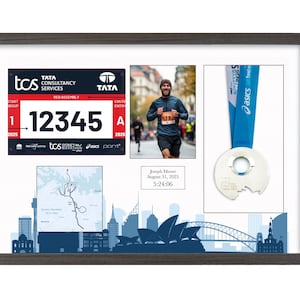 Può includere: Cornice con ricordi di maratona, tra cui un pettorale con il numero 12345, una foto di un corridore, una medaglia e una mappa del percorso. La cornice ha una finitura grigio scuro e presenta il testo "TCS Sydney Marathon".
