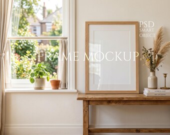 Könnte beinhalten: Ein Holzrahmen-Mockup mit dem Text "FRAME MOCKUP" steht auf einer rustikalen Holzbank. Die Szene umfasst ein Fenster mit natürlichem Licht, eine kleine Pflanze und dekorative Elemente, die eine gemütliche, einladende Atmosphäre schaffen.