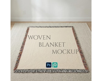 Könnte beinhalten: Eine beige gewebte Decke mit Fransen, die auf einem hellfarbigen Teppich liegt. Auf der Decke steht in Dunkelgrau "WOVEN BLANKET MOCKUP". Die Decke hat eine quadratische Form.