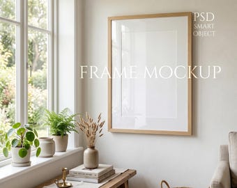 Könnte beinhalten: Ein großer, rechteckiger Holzrahmen-Mockup mit weißem Passepartout an einer hellen Wand. Der Text "FRAME MOCKUP" ist auf der Wand aufgedruckt. Der Rahmen ist von einem Fenster, Pflanzen, Büchern und einer Bank umgeben.