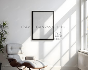 Könnte beinhalten: Ein gerahmter Leinwand-Mockup mit dem Text "FRAMED CANVAS MOCKUP" und "PSD SMART OBJECT" an einer weißen Wand. Ein moderner grauer Sessel mit braunem Sockel und Fußstütze steht auf einem Holzboden. Sonnenlicht scheint durch ein Fenster.