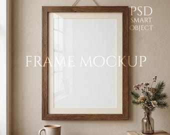 Könnte beinhalten: Ein rechteckiger Holzrahmen-Mockup mit dem Text "FRAME MOCKUP" und "PSD SMART OBJECT". Der Rahmen hängt an einer beigefarbenen Wand. Ein kleiner Tisch trägt eine Kaffeetasse, eine Blumenvase und ein Buch.
