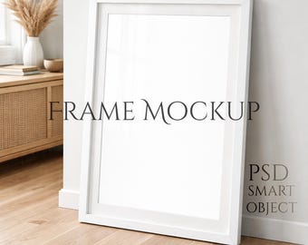 Könnte beinhalten: Ein großes weißes Bilderrahmen-Mockup, das an einer weißen Wand auf einem hellen Holzboden lehnt. Der Text "FRAME MOCKUP" wird auf dem Rahmen angezeigt. Der Text "PSD SMART OBJECT" wird an der Wand angezeigt. Ein kleiner Teppich liegt auf dem Boden.