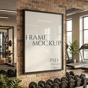Puede incluir: Una maqueta enmarcada con el texto "FRAME MOCKUP" y "PSD SMART OBJECT" en una pared de ladrillo. El marco es negro y el fondo incluye equipos de gimnasio y pesas.