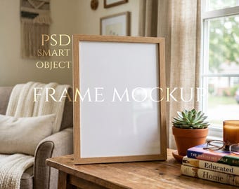 Könnte beinhalten: Ein Holz-Bilderrahmen-Mockup mit dem Text "FRAME MOCKUP" in Weiß. Der Rahmen steht auf einem Holztisch mit einer Sukkulente in einem Terrakotta-Topf, Büchern und einer Kerze. Der Hintergrund umfasst ein Fenster und ein Sofa.