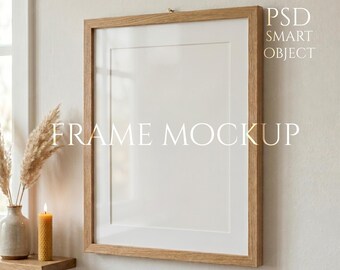 Könnte beinhalten: Ein rechteckiger Holzrahmen-Mockup mit weißem Passepartout, der an einer hellen Wand hängt. Der Rahmen hat eine natürliche Holzoberfläche. Der Text auf dem Bild lautet "FRAME MOCKUP" und "PSD SMART OBJECT". Ein Regal mit einer Vase, Trockenblumen und einer brennenden Kerze ist sichtbar.