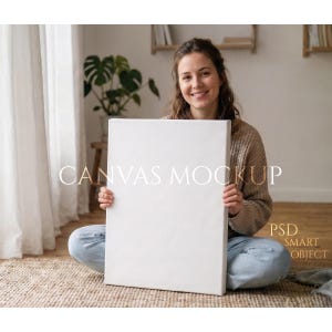 Puede incluir: Una persona sentada con las piernas cruzadas sostiene un lienzo blanco en blanco. El lienzo es rectangular y está estirado sobre un marco de madera. El texto en el lienzo dice "CANVAS MOCKUP" y "PSD SMART OBJECT". El fondo incluye una ventana, una planta y una alfombra.