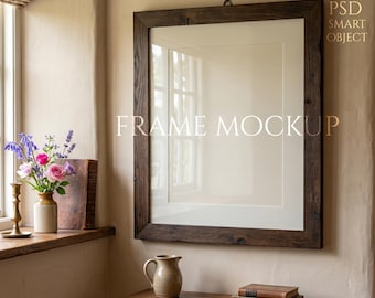 Könnte beinhalten: Ein großer, rechteckiger Holzrahmen mit weißem Passepartout hängt an einer beigefarbenen Wand. Der Rahmen ist dunkelbraun und hat ein rustikales, strukturiertes Aussehen. Der Text "FRAME MOCKUP" wird auf dem Rahmen angezeigt. Vor dem Rahmen steht ein kleiner Tisch mit einem Krug und Büchern.