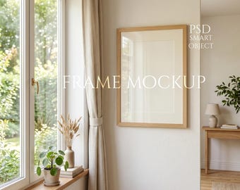 Könnte beinhalten: Ein gerahmtes Mockup mit dem Text "FRAME MOCKUP" und "PSD SMART OBJECT" in einem hellen Raum. Der Rahmen ist aus hellem Holz, und der Raum hat ein Fenster mit Blick ins Grüne, einen beigen Vorhang und einen kleinen Tisch mit einer Lampe.