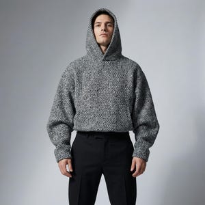 Op de afbeelding: Een grijs en wit gespikkelde hoodie met een relaxte pasvorm. De hoodie heeft een trekkoord en een kangoeroezak. Het model draagt een zwarte broek. De achtergrond is effen grijs.