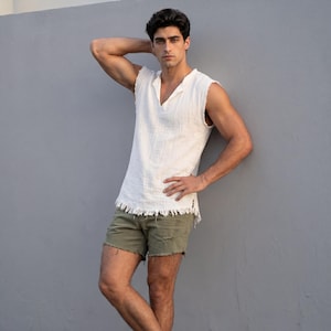 May include: A sleeveless white top with a V-neck and frayed edges, paired with olive green distressed shorts. The outfit is casual and summery, perfect for warm weather. The top has a textured appearance.