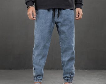Puede incluir: Pantalones deportivos de mezclilla azul claro con cintura con cordón y puños elásticos. Los pantalones tienen un corte relajado y se combinan con zapatillas blancas con detalles rojos. El modelo lleva una camisa negra de manga larga.