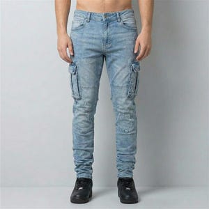 May include: Light blue denim cargo pants with multiple pockets on the thighs and knees. The jeans have a faded wash and distressed details. The pants are worn with black sneakers.