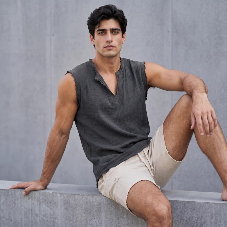 May include: A dark gray sleeveless shirt with a V-neck and frayed edges. Paired with light beige shorts with distressed details. The model is sitting on a concrete surface.