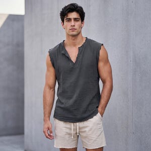 May include: A sleeveless, dark gray top with a V-neck and distressed edges, paired with beige shorts featuring a drawstring waist and frayed hems. The outfit is casual and relaxed.