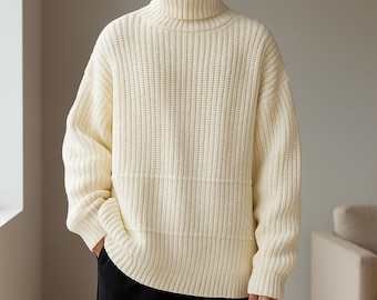 May include: Cream-colored turtleneck sweater with a ribbed knit design. The sweater has a relaxed fit and long sleeves. The model is wearing black pants. The sweater is made of a thick, warm material, perfect for cold weather.