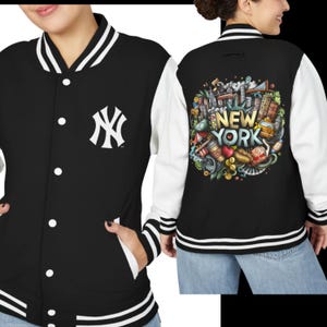 May include: Black and white varsity jacket with the New York Yankees logo on the front. The back features a colorful illustration with the words "New York" and iconic city imagery. The jacket has white sleeves and striped cuffs.