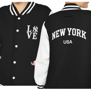 May include: Black and white varsity jacket with the text "LOVE" and a baseball team logo on the front. The back of the jacket features the words "NEW YORK" above "USA". The jacket has white sleeves and a button-up front.