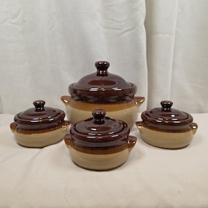 May include: A set of four ceramic brown and tan lidded bowls. The bowls vary in size, with the largest in the center and the smallest in the front. Each bowl has a dark brown lid and a light tan base with a brown band.