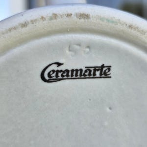 May include: Close-up of a white ceramic object with the black text "Ceramarte" and the number "52" printed on the surface. The object has a slightly textured surface.