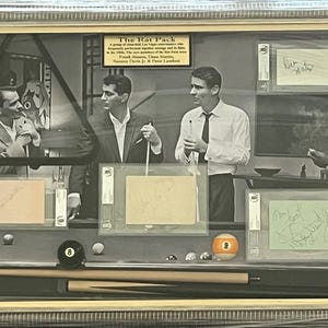 Peut inclure: Photographie encadrée en noir et blanc représentant The Rat Pack, avec Frank Sinatra, Dean Martin, Sammy Davis Jr. et Peter Lawford. L'image comprend un billard avec des boules et des queues, et plusieurs articles signés.