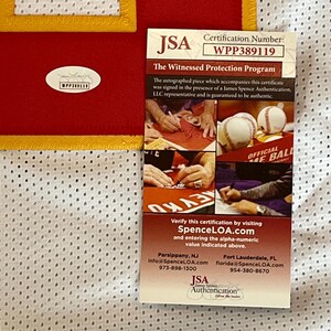 May include: A red and white jersey with a yellow trim, accompanied by a JSA authentication certificate. The certificate displays the certification number WPP389119 and details about the witnessed autograph program.