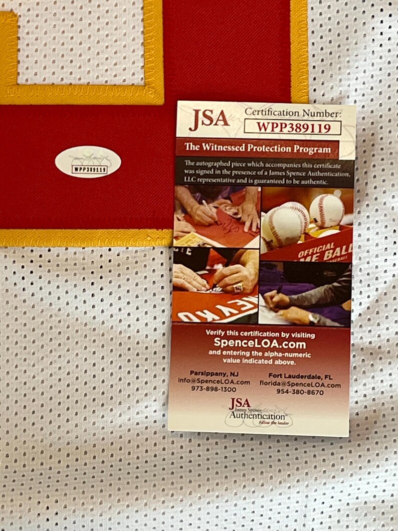 May include: A red and white jersey with a yellow trim, accompanied by a JSA authentication certificate. The certificate displays the certification number WPP389119 and details about the witnessed autograph program.