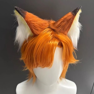Può includere: Orecchie da volpe arancioni con punte nere e pelliccia bianca all'interno, attaccate a una parrucca arancione. Presentate su una testa di manichino, ideali per cosplay o eventi in costume.
