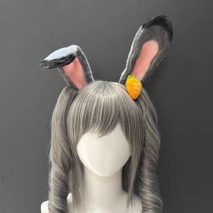 Può includere: Fascia per capelli con orecchie da coniglio grigie con interno rosa e un piccolo accento di carota arancione. Le orecchie soffici sono dritte e la fascia è indossata su una testa di manichino con trecce grigie. Un accessorio divertente per cosplay o eventi a tema.