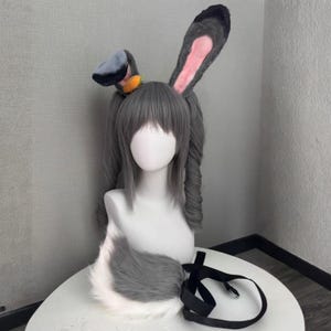 Può includere: Una parrucca grigia con lunghe code di cavallo, orecchie da coniglio e una coda soffice. Le orecchie da coniglio sono grigie con l'interno rosa. Un nastro nero con una fibbia argentata è attaccato alla coda. Una piccola carota arancione è sulla testa.