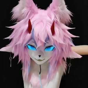 May include: A pink and white furry mask with glowing blue eyes and small red horns. The mask has long, pointed ears and a stylized cat-like face. The mask is a cosplay item.