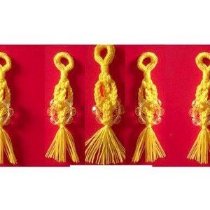 May include: Five yellow macrame keychains, each with a loop, beaded section, and tassel. They are set against a red background. The keychains are handmade.