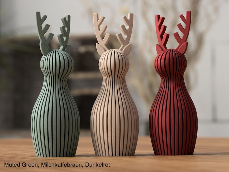 Pu&ograve; includere: Tre statuette di renne stilizzate con un design a coste verticali. La figura a sinistra &egrave; verde tenue, quella centrale &egrave; beige e quella a destra &egrave; rosso scuro. Ogni renna presenta palchi prominenti e una forma del corpo liscia e arrotondata.