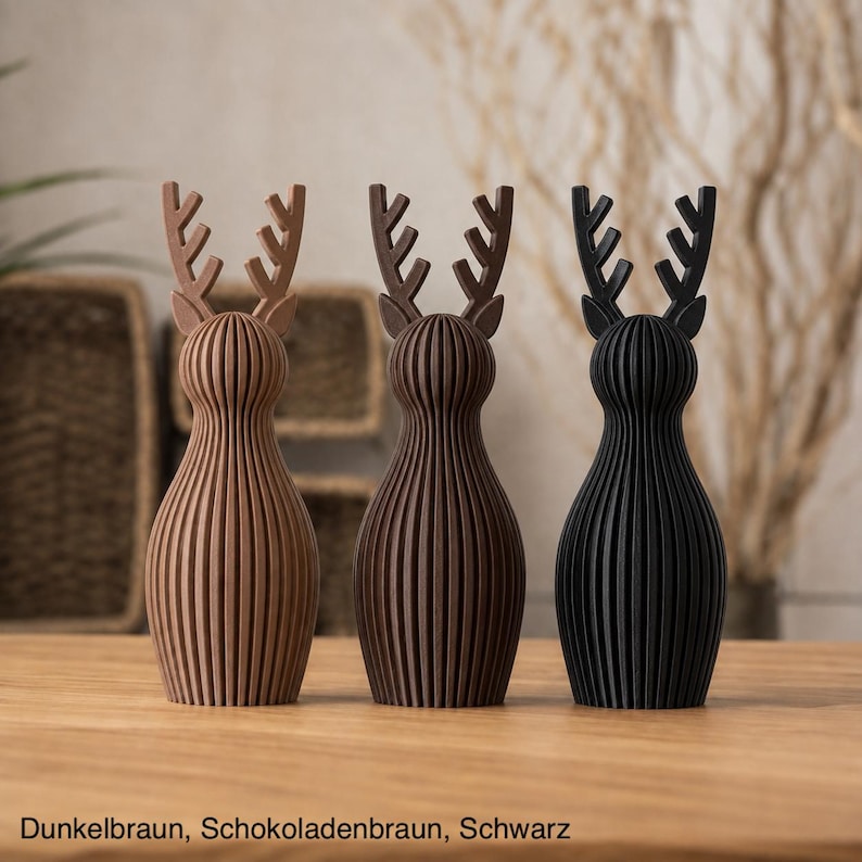 Pu&ograve; includere: Tre statuette di cervo in piedi con corpi a linee verticali scanalate e corna ramificate. Le figure sono disposte in fila, colorate in marrone chiaro, marrone cioccolato scuro e nero, con il testo Dunkelbraun, Schokoladenbraun, Schwarz.