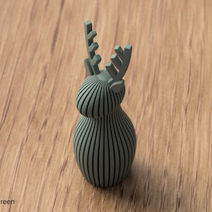 Pu&ograve; includere: Una statuetta di cervo color verde tenue costruita con una serie di listelli verticali e paralleli che formano un corpo e una testa arrotondati, sormontati da due palchi stilizzati. L'oggetto presenta una finitura opaca uniforme.