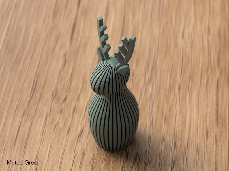 Pu&ograve; includere: Una statuetta di cervo color verde tenue costruita con una serie di listelli verticali e paralleli che formano un corpo e una testa arrotondati, sormontati da due palchi stilizzati. L'oggetto presenta una finitura opaca uniforme.