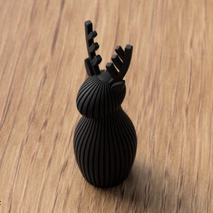 Pu&ograve; includere: Una statuetta nero opaco a forma di cervo con una texture a coste verticali che copre il corpo arrotondato, la testa e le corna. L'oggetto presenta una base solida e liscia con una finitura scura uniforme su tutta la sua struttura.